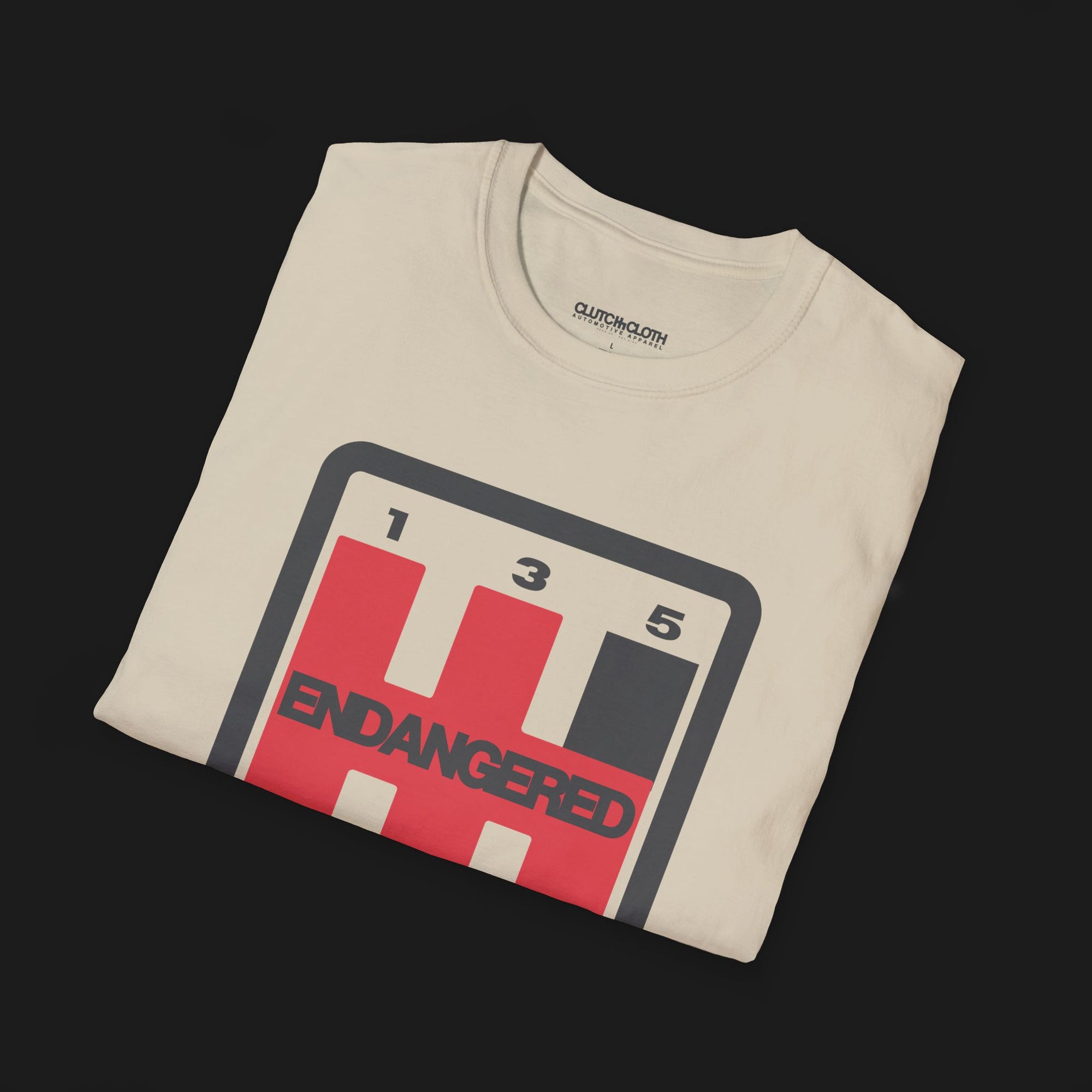 Folded Endangered Species Shifter Automotive Graphic T-Shirt – Sand unisex tee featuring a bold manual gear shift design with 'Endangered' text. A perfect gift for stick shift enthusiasts and car lovers.