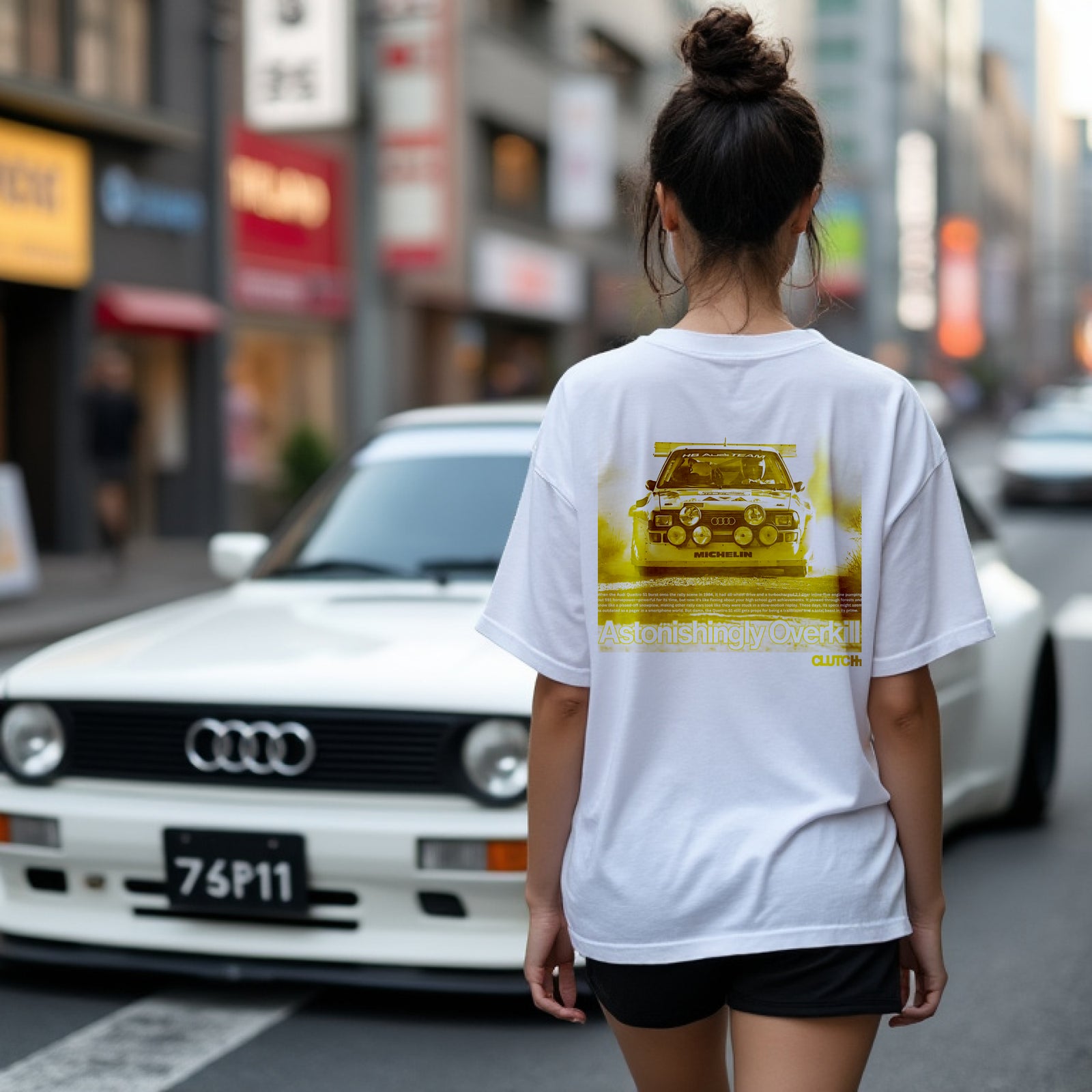 Women wearing the Astonishingly Overkill Automotive Graphic T-Shirt – White tee featuring a bold Audi Quattro rally car design with a yellow overlay and "Astonishingly Overkill" text. Perfect gift for rally fans and car enthusiasts.