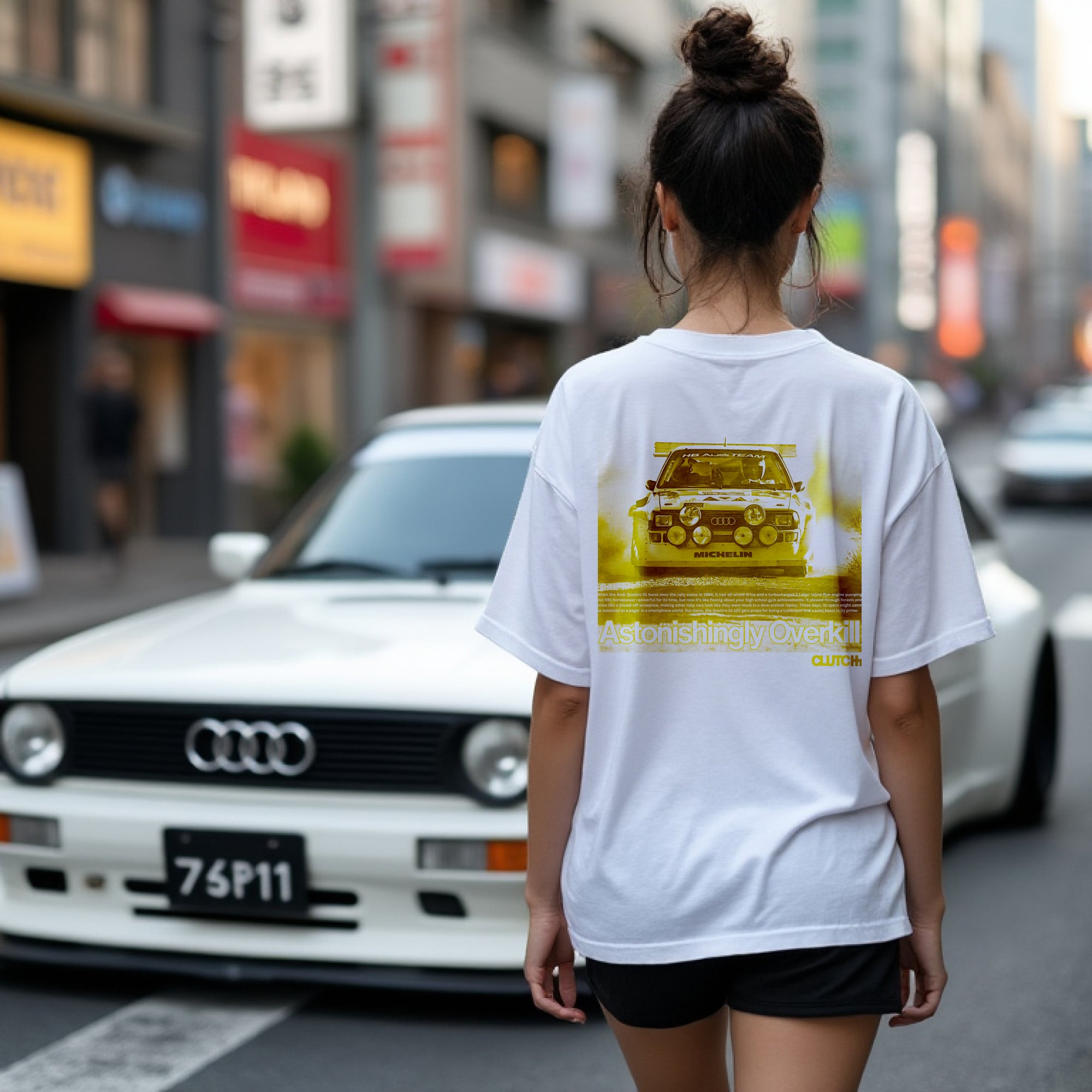 Women wearing the Astonishingly Overkill Automotive Graphic T-Shirt – White tee featuring a bold Audi Quattro rally car design with a yellow overlay and "Astonishingly Overkill" text. Perfect gift for rally fans and car enthusiasts.