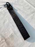 Black keychain strap with text on a light gray background