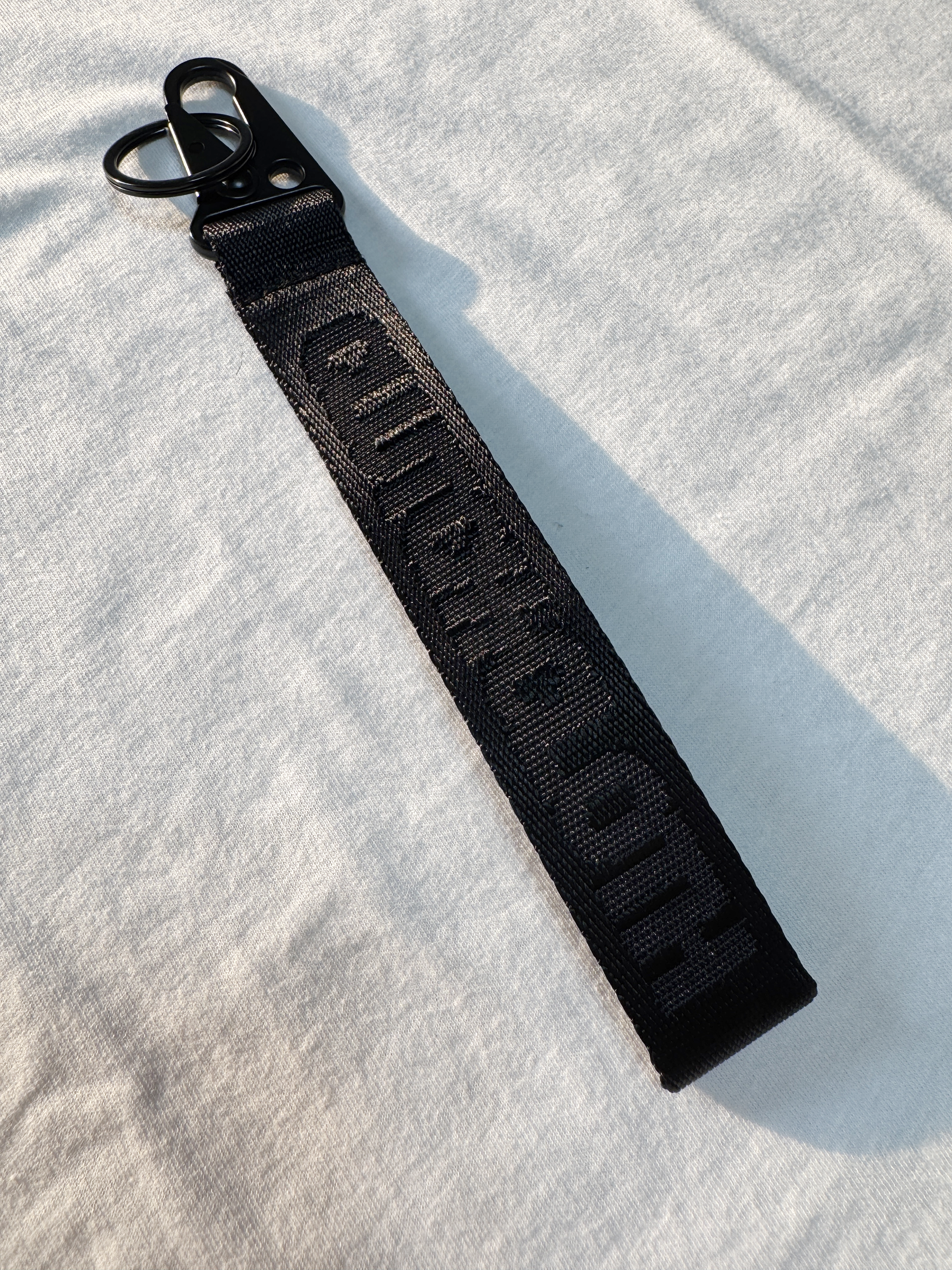 Black keychain strap with text on a light gray background