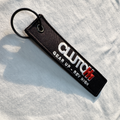 Black keychain with 'CLUTCH' branding on a light gray fabric background