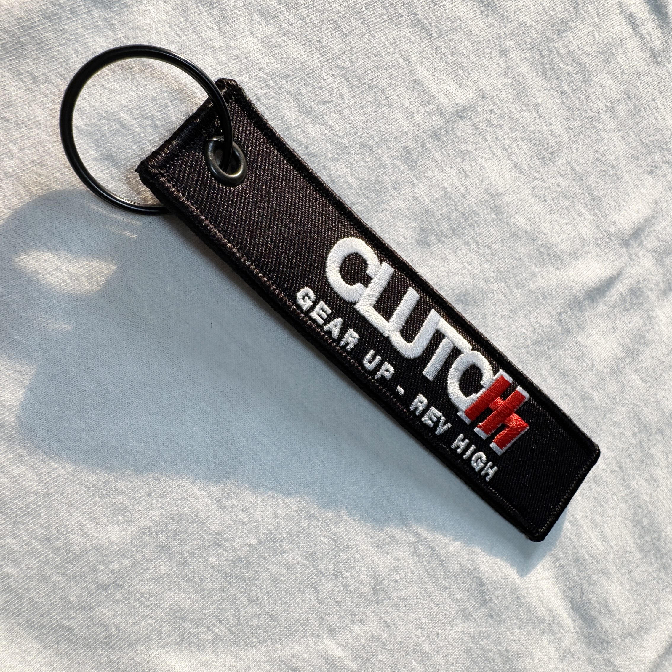 Black keychain with 'CLUTCH' branding on a light gray fabric background