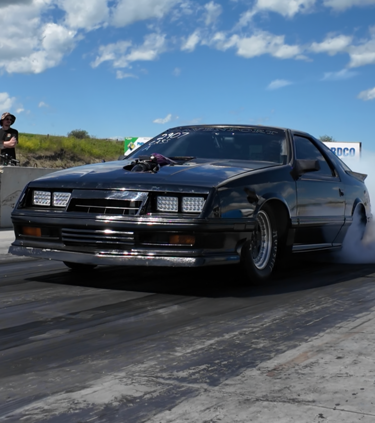 Black car on a racetrack with a blue sky and clouds in the background