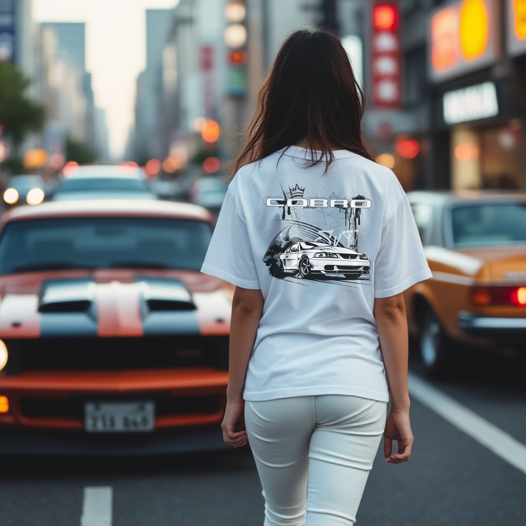 Woman wearing Cobro x Clutch Automotive Graphic T-Shirt – Blue tee featuring a detailed white Mustang Cobra design with graffiti-style background and "Cobro" text. Perfect gift for Mustang fans and car enthusiasts.