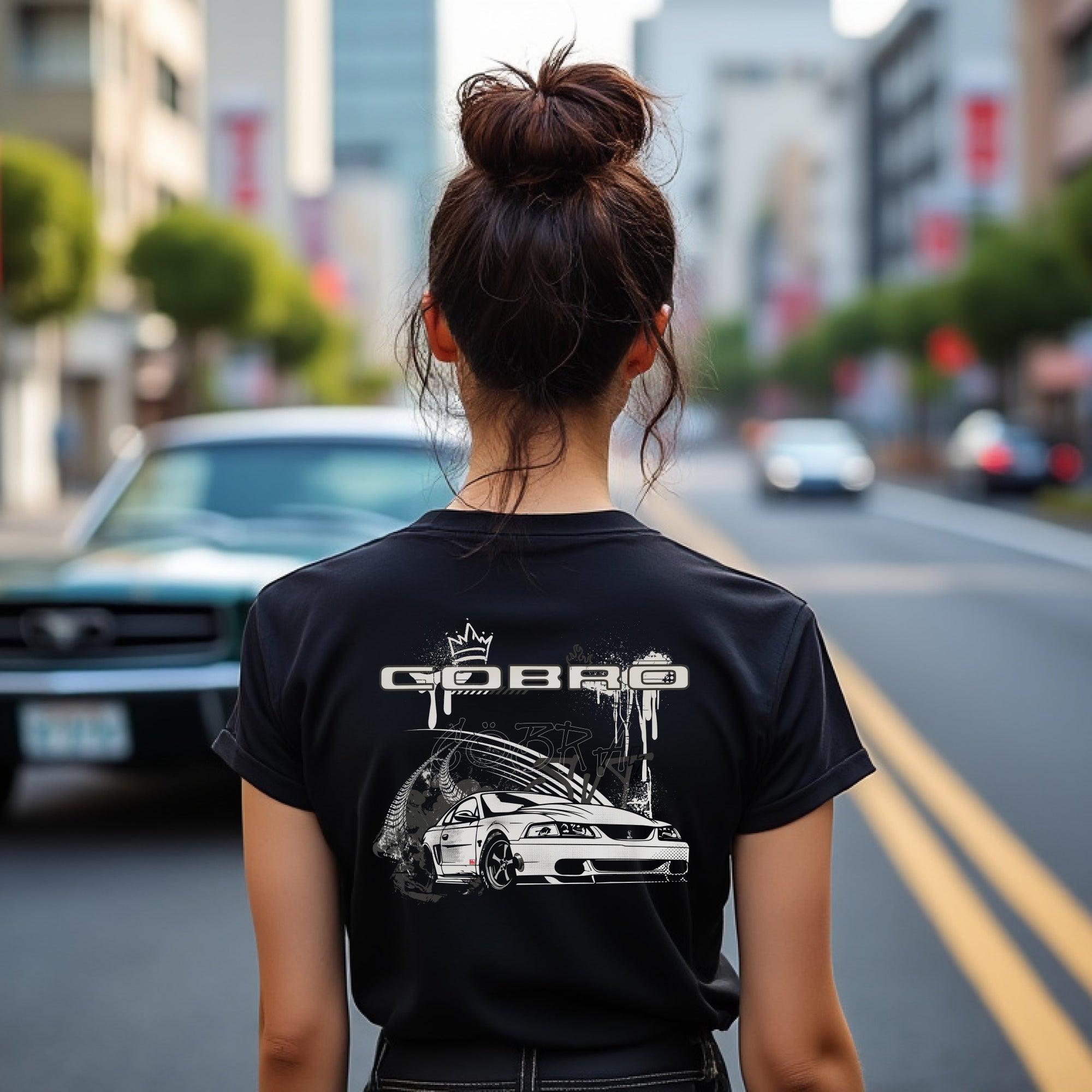 Woman wearing Cobro x Clutch Automotive Graphic T-Shirt – Black tee featuring a detailed white Mustang Cobra design with graffiti-style background and "Cobro" text. Perfect gift for Mustang fans and car enthusiasts.