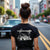 Woman wearing Cobro x Clutch Automotive Graphic T-Shirt – Black tee featuring a detailed white Mustang Cobra design with graffiti-style background and "Cobro" text. Perfect gift for Mustang fans and car enthusiasts.