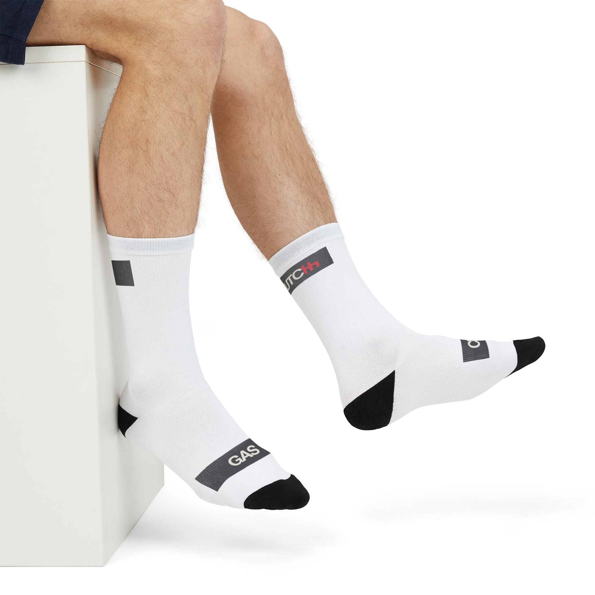 Man seated wearing Driving Lessons Crew Socks – White and black unisex crew socks featuring "GAS" and "CLUTCH" labels on the toes and heel. Comfortable and stylish, designed for automotive enthusiasts. Ideal gift or stocking stuffer for men and women who love cars and driving culture
