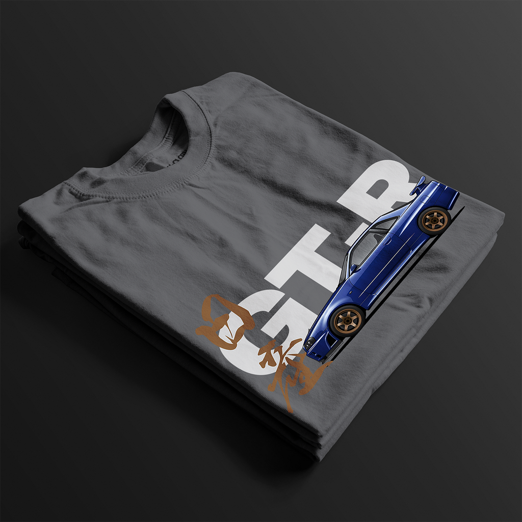 Folded Charcoal R34 GT-R Automotive Graphic T-Shirt featuring a blue Nissan Skyline with gold accents and Japanese calligraphy design, unisex car enthusiast gift