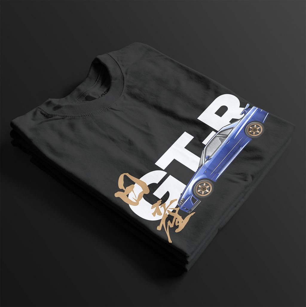 Folded Black R34 GT-R Automotive Graphic T-Shirt featuring a blue Nissan Skyline with gold accents and Japanese calligraphy design, unisex car enthusiast gift